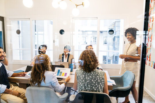 Group of diverse professionals actively meeting in a boardroom, discussing charts and presentations in a contemporary coworking space