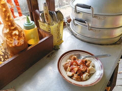 Traditional Indonesian siomay street food cart with steamed dumplings, peanut sauce, condiments, and aluminum steamer. Authentic local culinary scene at a roadside food stall.