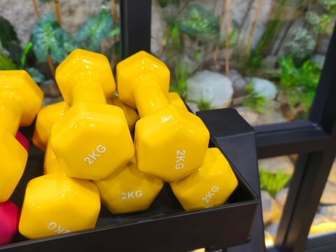 close-up of a neat stack of vibrant yellow 2kg vinyl-coated hexagonal dumbbells resting securely on a black metal storage rack