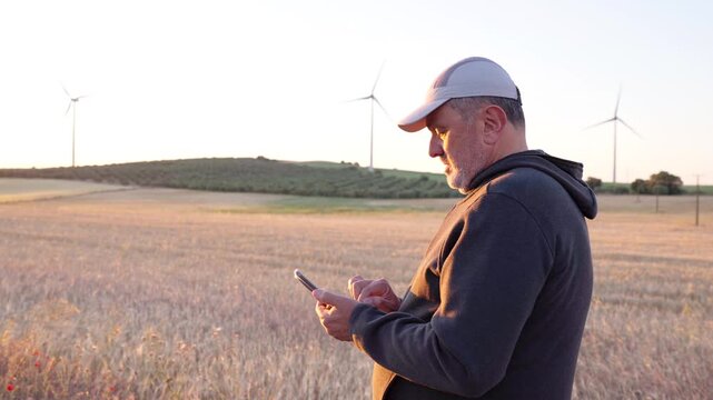 Farmer using a smartphone in a wheat field with wind turbines