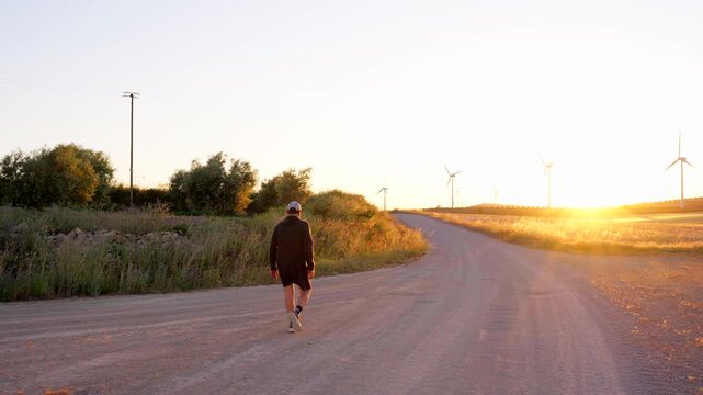 Man walking on a country road towards wind turbines at sunset