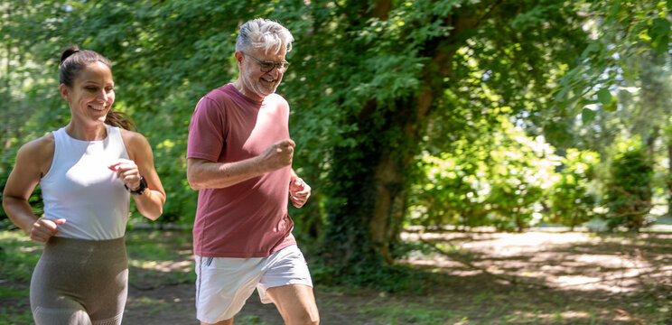 Jogging senior man with female fitness coach exercising outdoors in a park, promoting active aging, wellness, cardio training and healthy lifestyle.