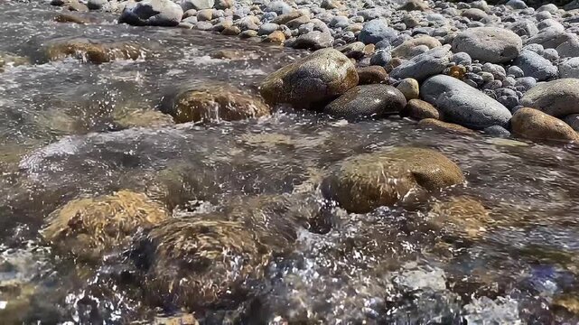 Clear fresh water stream flowing over smooth rocks and pebbles in a mountain river
