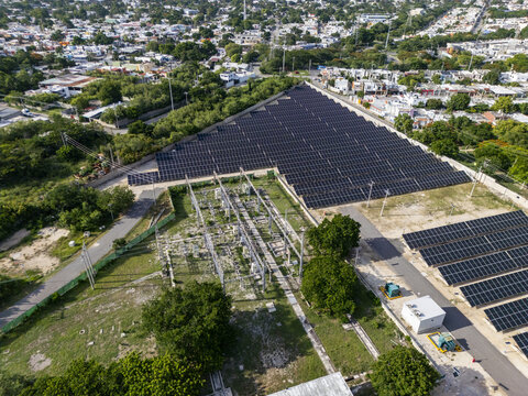 Aerial view of a solar power plant with rows of photovoltaic panels and an electrical substation, situated within the urban landscape of Merida, Yucatan, Mexico.