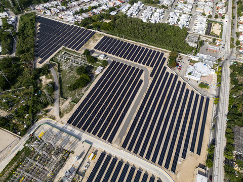 Aerial view of a solar power plant with rows of photovoltaic panels and an electrical substation situated within an urban residential area in Merida, Yucatan, Mexico.