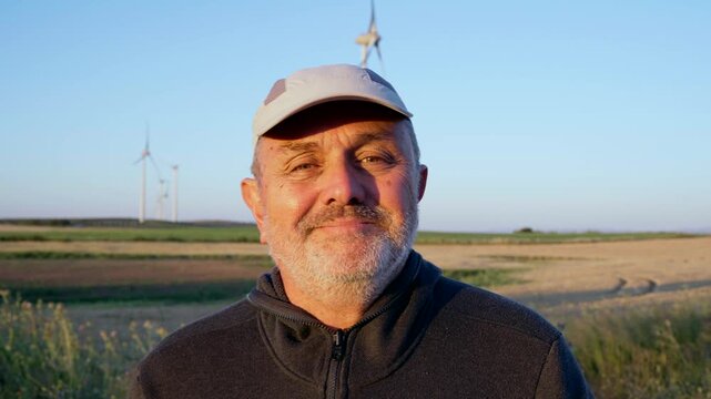 Mature farmer posing in a wind turbine field at sunset
