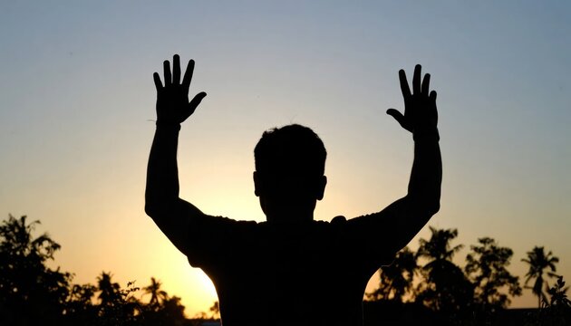 Silhouette of a man with arms raised at sunset.