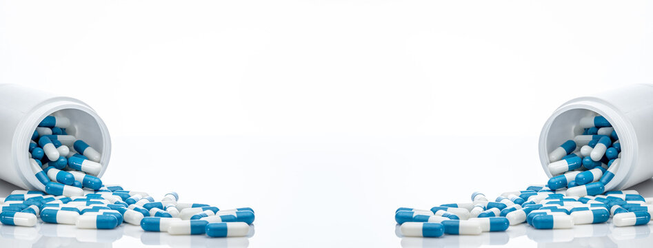 Blue-white antibiotic capsule pills spread out of plastic drug bottles. Antibiotic drug resistance. Prescription drugs. Healthcare and medicine. Pharmaceutical industry. Pharmacy product. Medication.