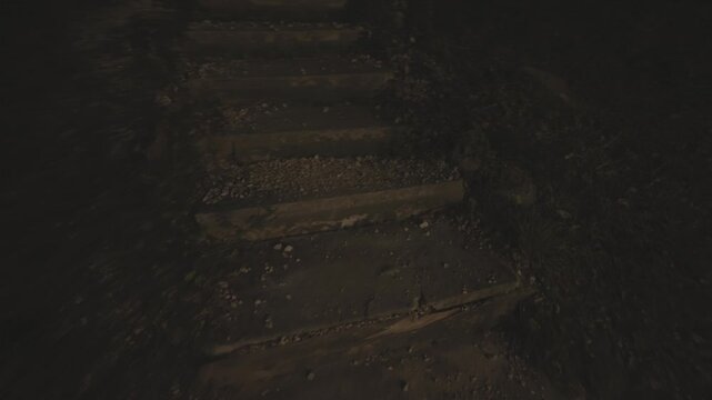 First person perspective of walking up a worn concrete staircase outdoors at night, with dirt and pebbles scattered on the steps in the dark