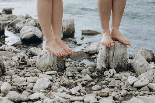 Couple's bare feet balancing on wooden stumps by water