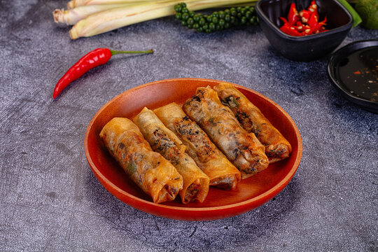 Crispy fried spring rolls on wooden plate with fresh chili and dipping sauce