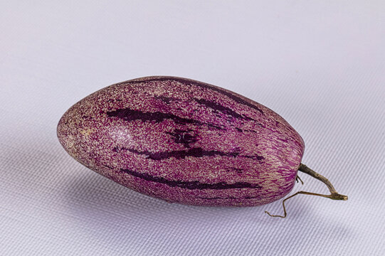 Whole ripe pepino melon with purple stripes on white textured background