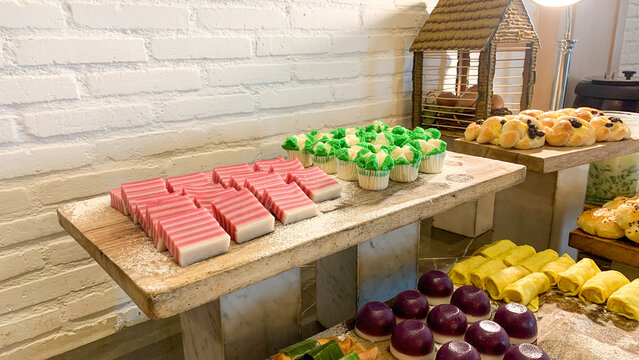 Traditional Indonesian market snacks, known as jajanan pasar, displayed in colorful varieties on rustic wooden shelves. The assortment of traditional cakes and sweet treats represents Indonesian