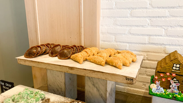 panada cake and cucur cake from indonesia, Assorted freshly baked pastries and bread arranged on a rustic wooden display shelf in a cozy bakery or caf&eacute; interior. The selection includes golden-brown 