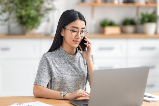 Smiling Asian woman talking on phone laptop