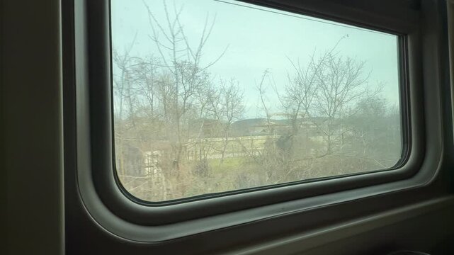 Rural landscape view from a moving train window passing small houses and trees. Eye level tracking shot.