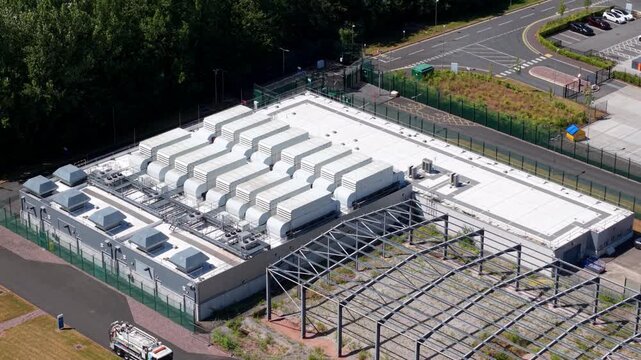 Aerial view of a data center facility with rows of industrial ventilation units on the roof, surrounded by security fencing and parking in Birmingham, England, United Kingdom.