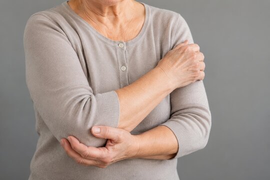 Elderly woman with arm pain touching painful elbow. Senior female suffering from elbow joint discomfort and inflammation. Medical concept of arthritis, orthopedic injury, aging health.