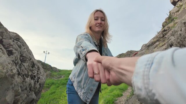 Point of view shot of a young woman reaching out and giving a helping hand to her partner while climbing up a rocky hill, symbolizing support, trust, and teamwork in a relationship