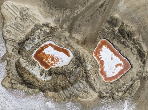 Aerial view of Skeleton Coast showing two distinct salt pans with reddish water and white mineral deposits surrounded by arid desert terrain in Dorob National Park, Kunene Region, Namibia.