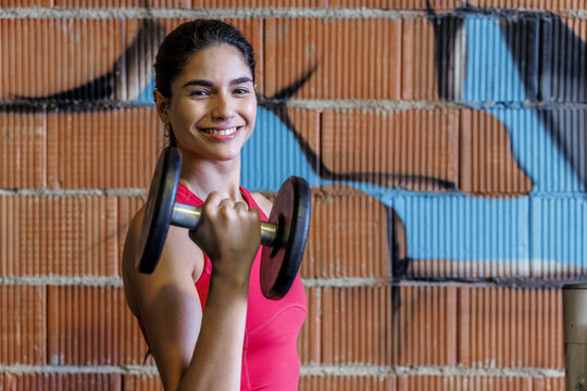 Woman lifting dumbbells in gym with graffiti wall