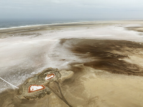 Aerial view of the Skeleton Coast salt pans with distinctive reddish pools and white salt crusts stretching towards the Atlantic Ocean, Dorob National Park, Kunene Region, Namibia.