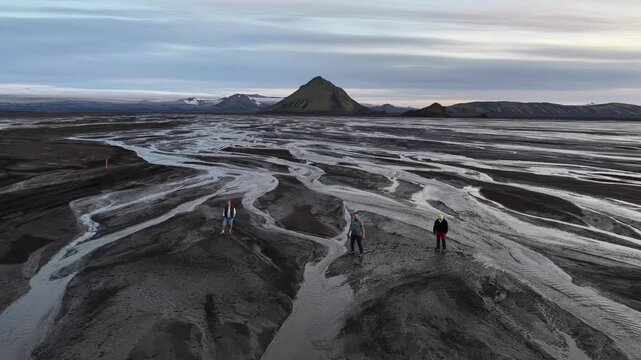 Aerial view of Maelifell volcano surrounded by dark volcanic sand and braided river channels with three people standing on the terrain in Skaftarhreppur, Iceland.