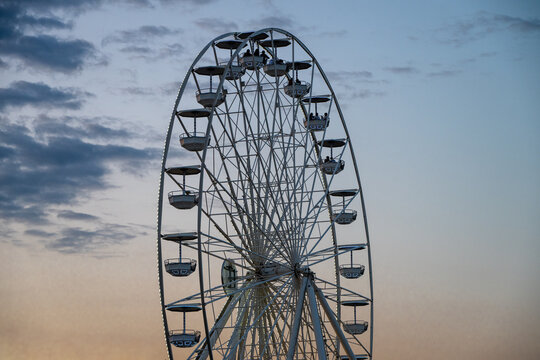 A large white Ferris wheel stands tall against a cloudy evening sky at dusk.