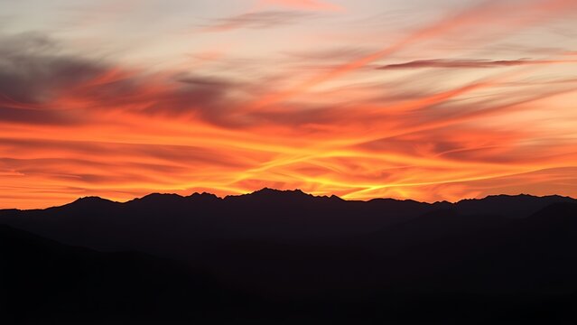 Dramatic sunset with orange hues over a silhouetted mountain range.