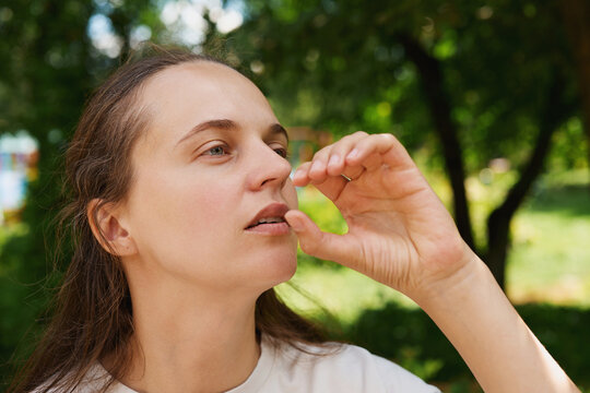 A woman is engaged in sign language, gesturing with her hand near her face in a park. The trees and grass are bright and clear around her while she focuses on communication