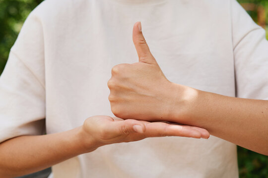 Hands show sign language gestures in a green area during the day. One hand gives a thumbs up while the other supports it