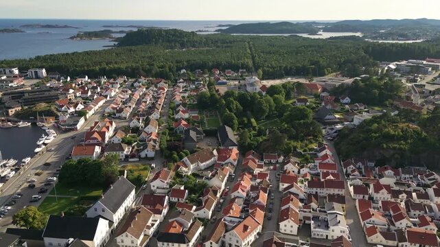 Aerial view of the coastal town of Mandal with its characteristic white wooden houses, red roofs, harbor with boats, and lush green surroundings in Mandal, Agder, Norway.