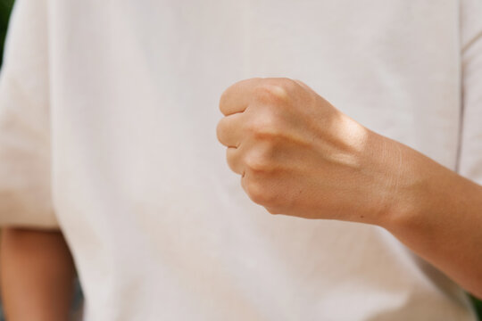 A person stands in a garden using sign language during the day. The focus is on a clenched fist, part of a sign meaning something specific