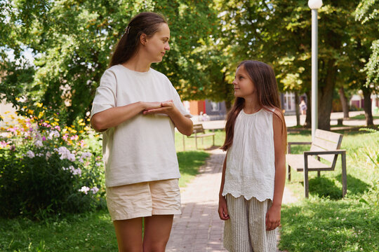 Two individuals are engaged in a conversation using sign language while walking through a park. They are next to flowering plants and benches