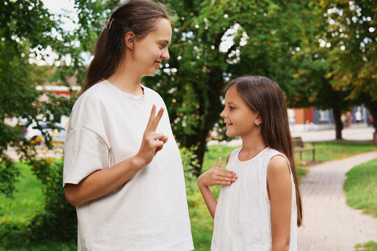 An adult teaches a child different signs in a park setting. They are focused and engaged, sharing smiles while learning. Trees surround them