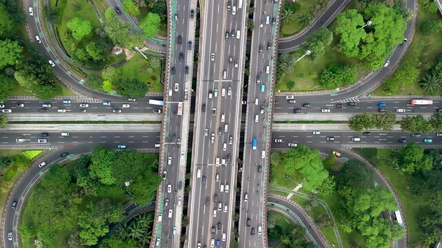 Aerial view of a busy highway interchange with multiple lanes and surrounding green trees in Jakarta, Indonesia.