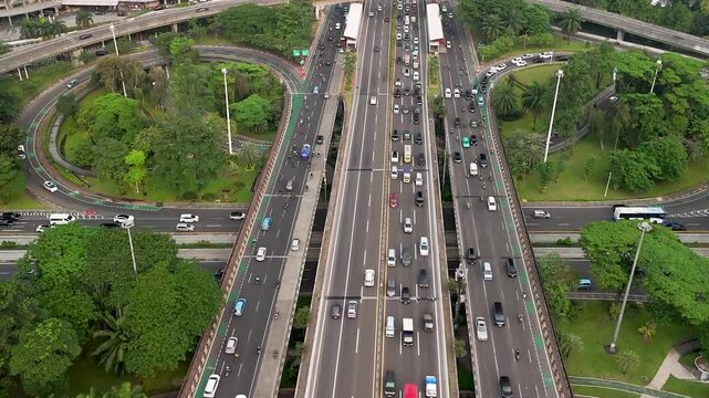 Aerial view of busy highway interchange with heavy traffic surrounded by lush green trees and elevated roads in Jakarta, Indonesia.