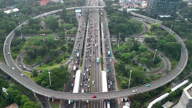 Aerial view of the Semanggi Interchange with heavy traffic flowing through the multi-level highway junction surrounded by lush green trees and urban infrastructure in Jakarta, Indonesia.