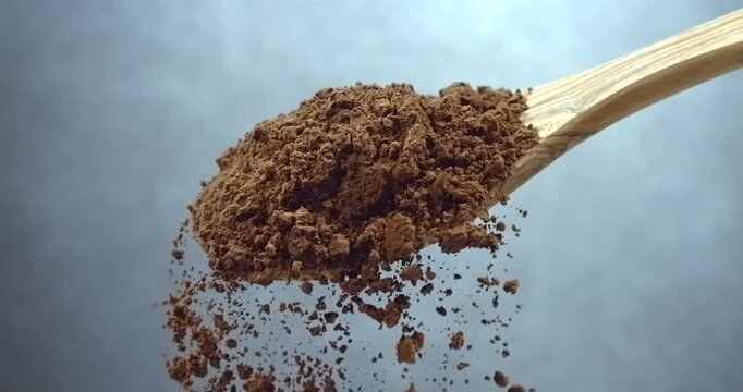 Cocoa powder falling from wooden spoon chocolate dust cloud slow motion