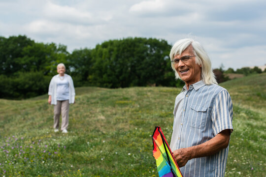 Joyful senior couple enjoys flying a colorful rainbow kite in a sunny meadow