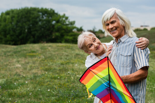 Joyful senior couple embraces freedom while flying a rainbow kite together