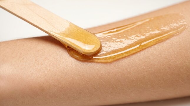 Applying warm sugar wax paste on arm with wooden spatula for hair removal epilation