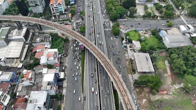 Aerial view of the Jakarta MRT line elevated track crossing over a busy multi-lane highway with heavy traffic and surrounding urban development in Cilandak, Jakarta, Indonesia.