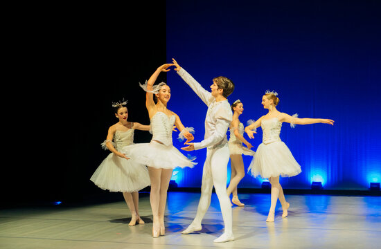 Ballet dancers perform a classical routine on stage with blue lighting
