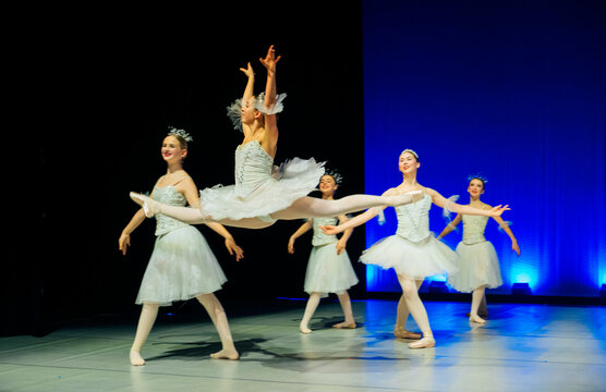 Ballet dancer performing a grand jet&eacute; leap on stage during recital