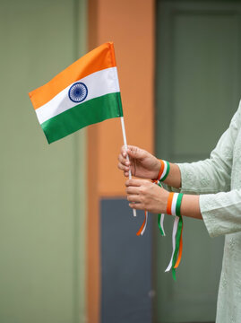 India Independence Day Woman Holding Small Indian Tricolor Flag in Hand with Orange White Green Ribbon Bracelet, Green Wall Background, Patriotic Close Up Concept for Republic Day Celebration
