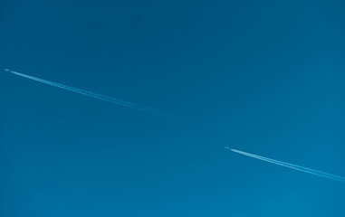 Two commercial airplanes flying with white condensation trails across clear blue sky. Aviation, global transportation, international travel, flight routes and air traffic. Airline transportation. © Fahroni
