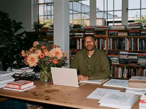 Young Creative Man Working on Laptop at Messy Desk in Bright Office Studio