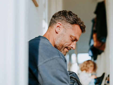 Smiling father helping his young child get ready in the hallway at home, authentic involved fatherhood and everyday family moment.