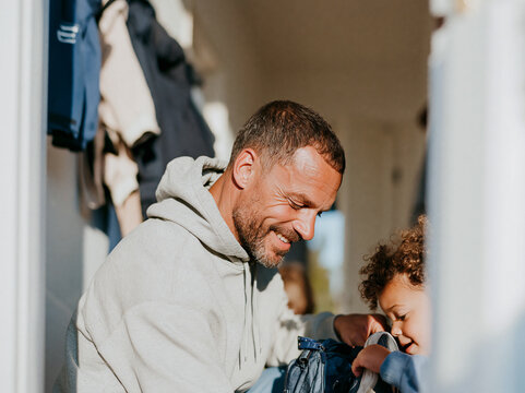 Smiling father helping his young child get ready in the hallway at home, authentic involved fatherhood and everyday family moment.